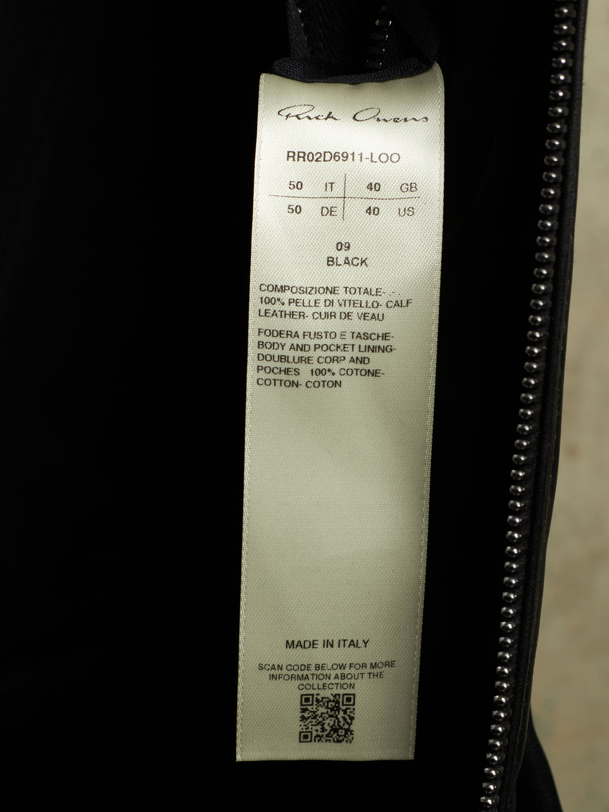 A close-up of a garment's interior label reading 'Ruffwax' and 'RR02D6911-LOO', size 50/50, black, with a zipper running along the right side.