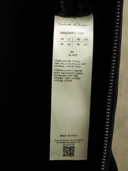 A close-up of a garment's interior label reading 'Ruffwax' and 'RR02D6911-LOO', size 50/50, black, with a zipper running along the right side.