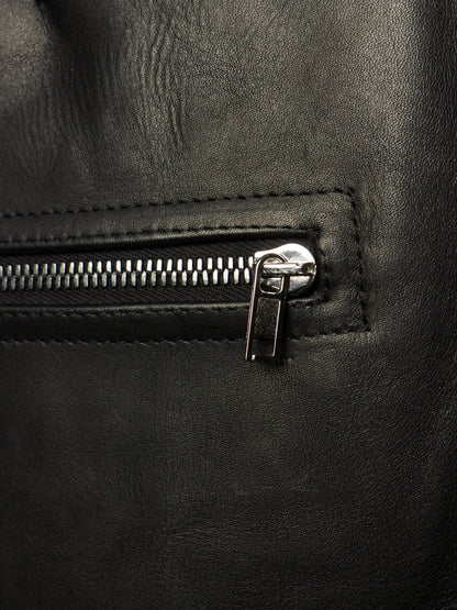 Close-up of a black leather backpack or bag featuring a silver metal zipper with a pull tab, set against a dark textured leather background.