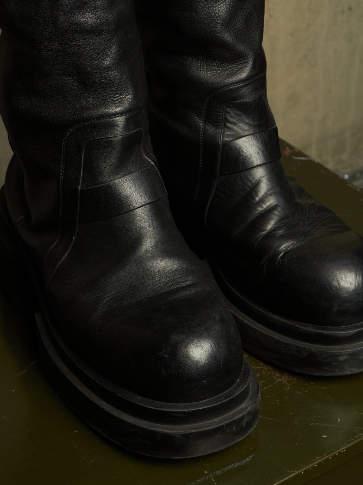 A close-up shot of a pair of black leather boots with chunky platform soles, resting on a dark green surface.