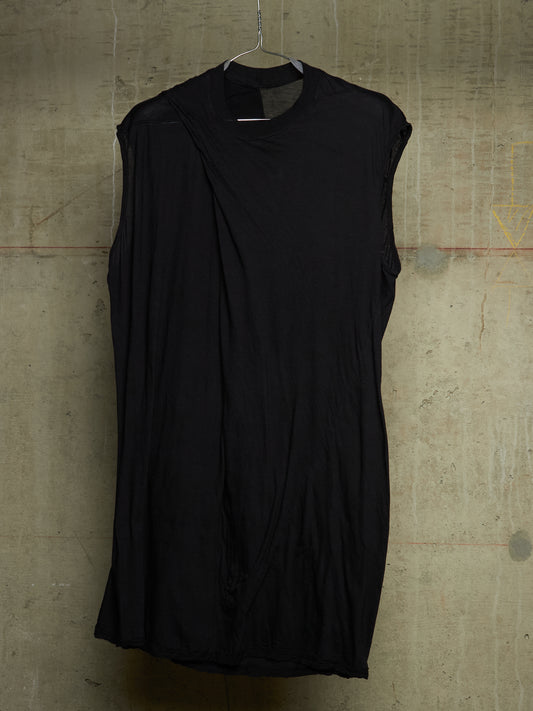 A black sleeveless draped dress with a mock neck, hanging on a metal hanger against a textured concrete wall.