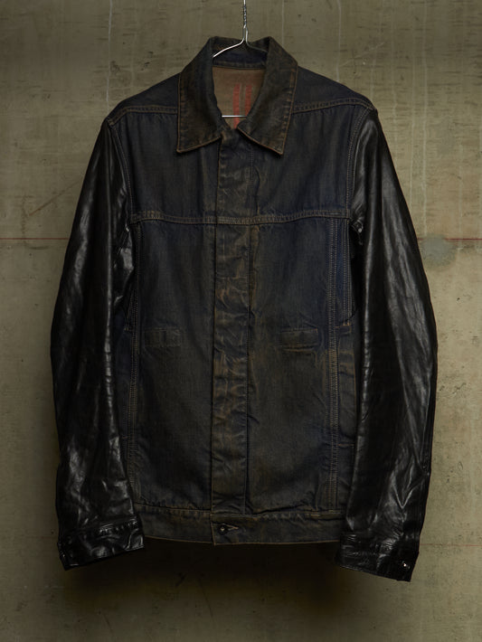 A dark brown leather jacket with a collar and front button closure, hanging against a textured concrete wall.