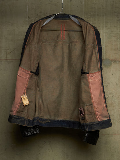 A vintage-style patchwork jacket hanging on a wire hanger against a textured concrete wall. The jacket features a brown canvas body with dusty pink patchwork pockets, dark navy blue denim trim, and red stitching details.