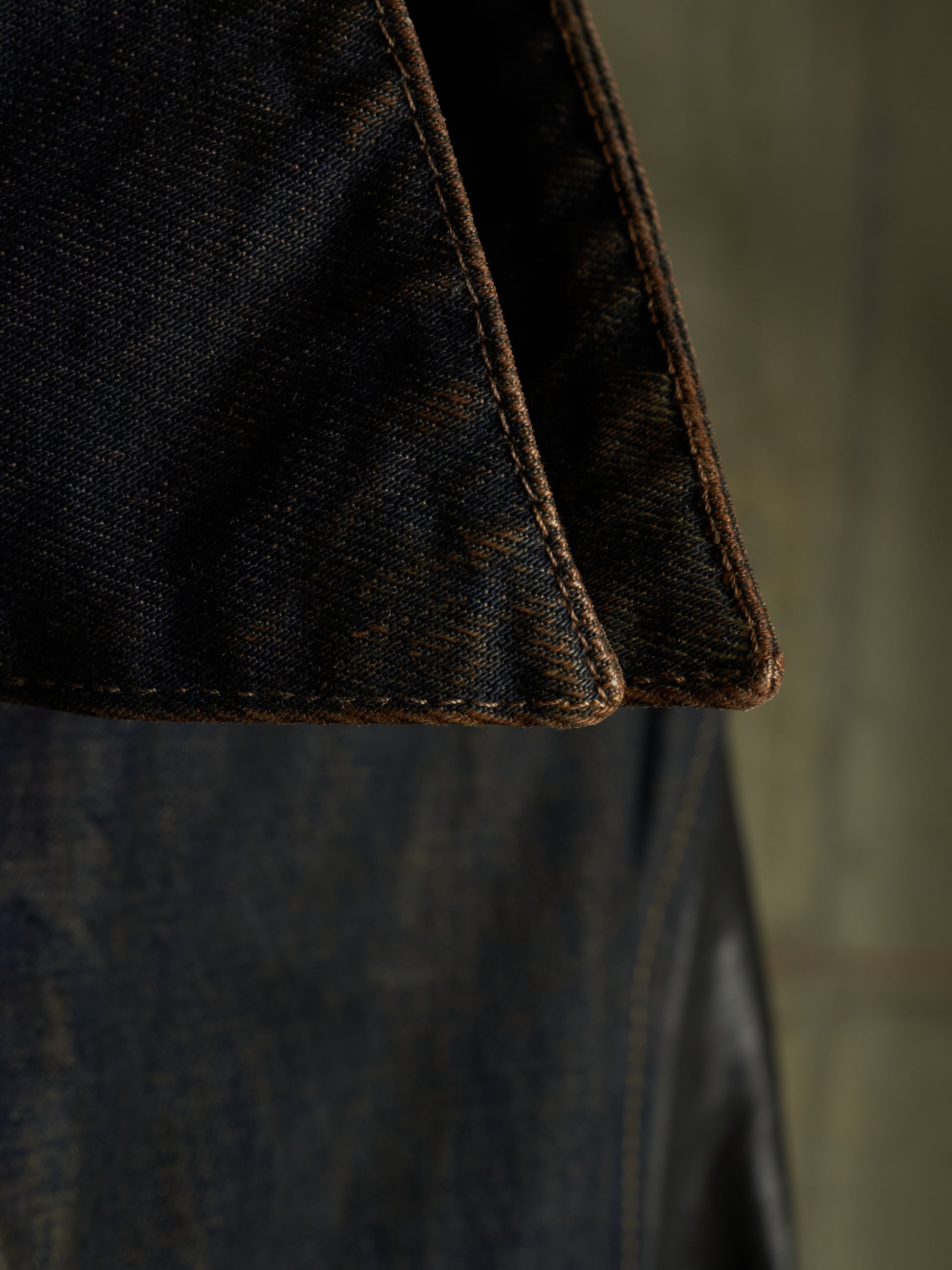 Close-up detail of dark indigo denim fabric with contrast brown stitching along folded seams.