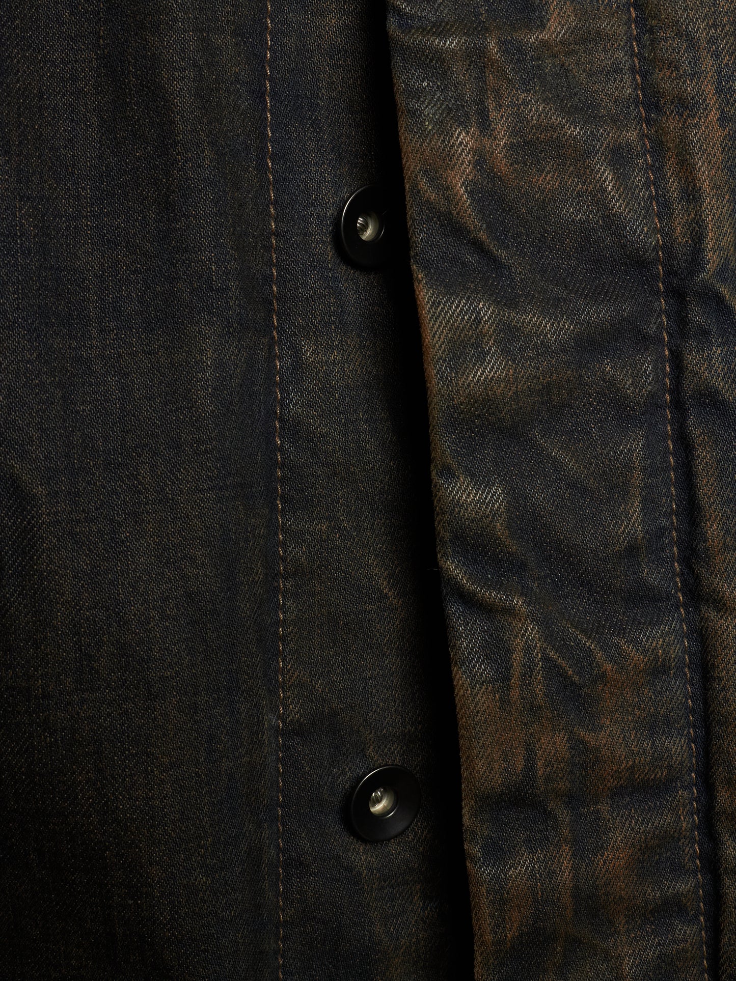 Close-up of a dark textured button-up shirt with a heavily distressed, mottled finish in black and brown tones.