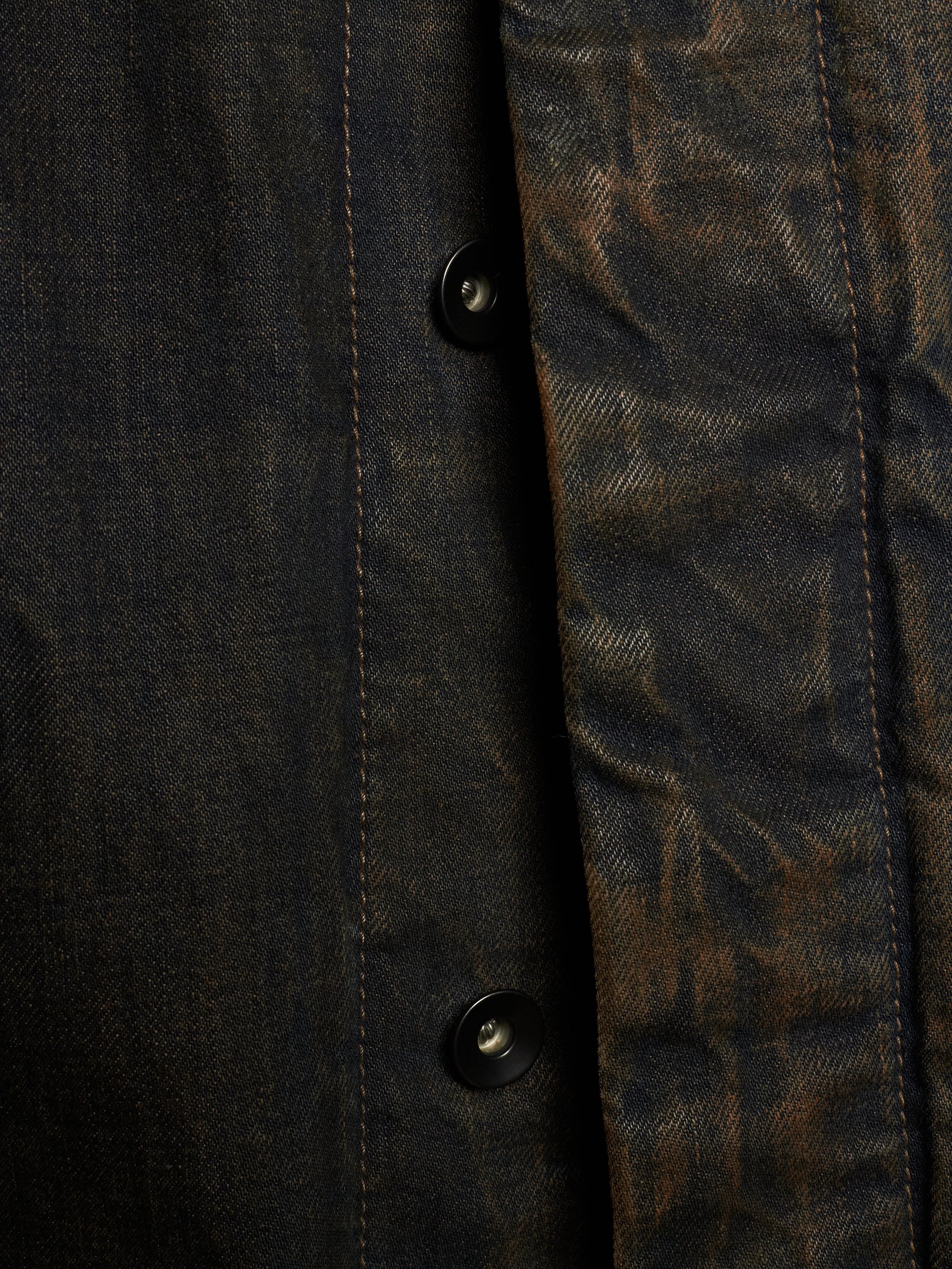 Close-up of a dark textured button-up shirt with a heavily distressed, mottled finish in black and brown tones.
