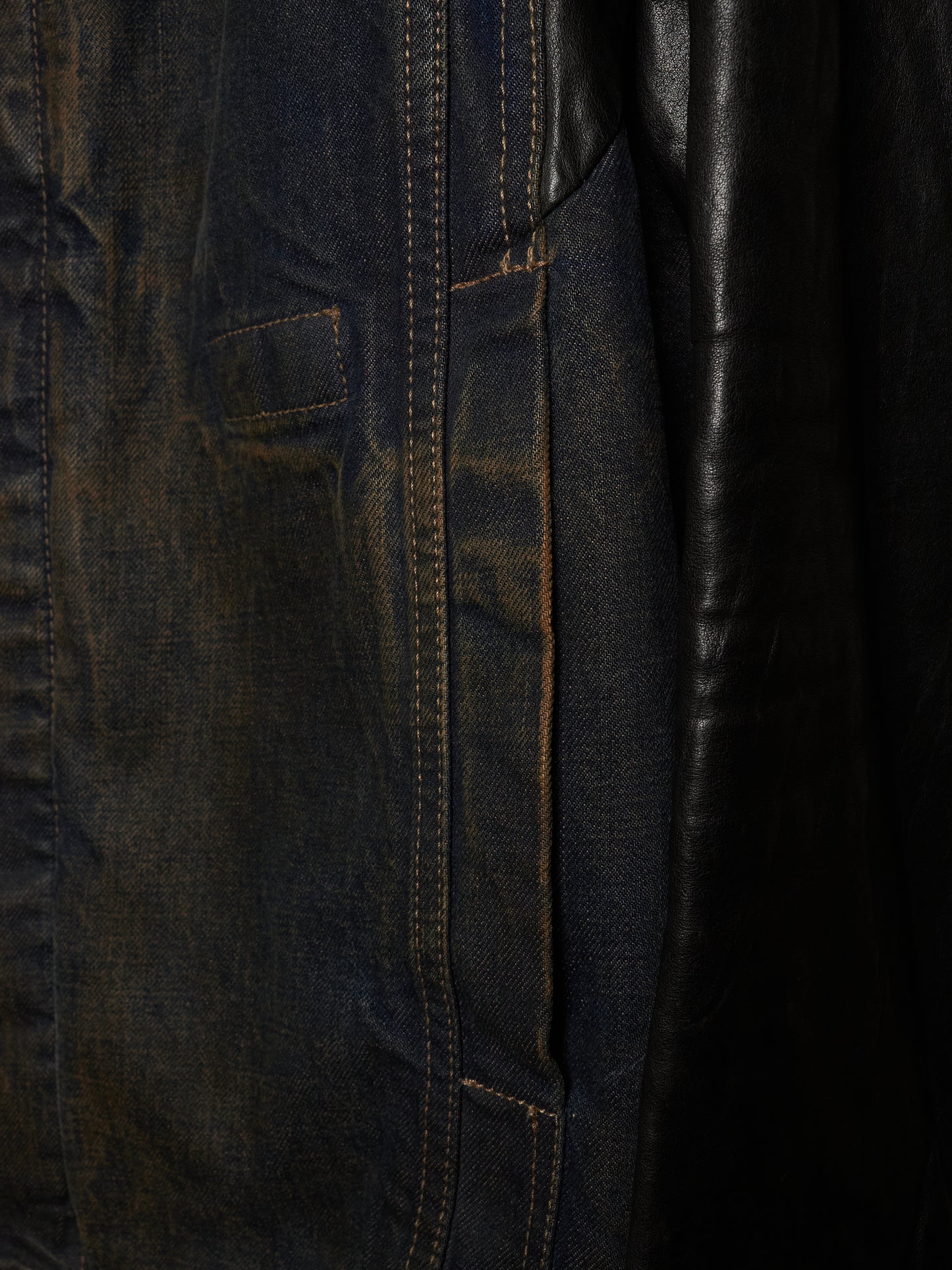 Close-up detail of a dark indigo denim jacket with contrast stitching and a black leather panel.
