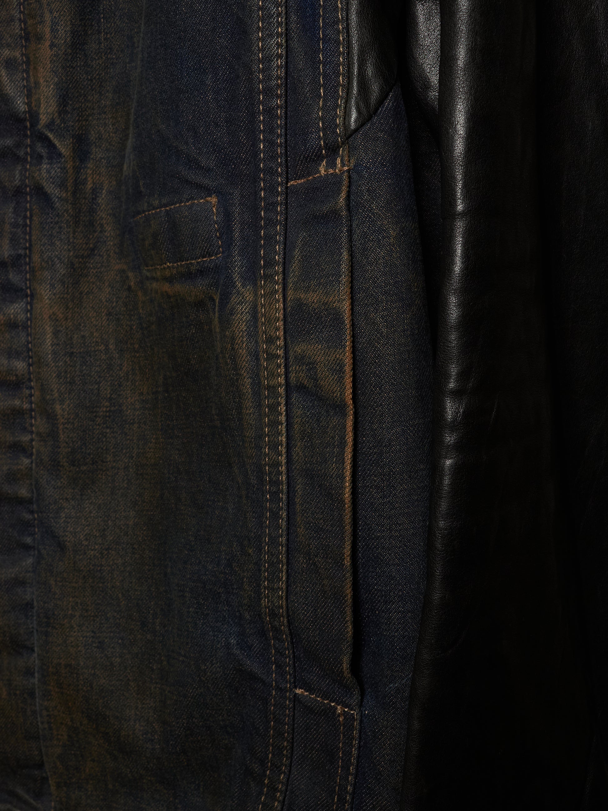 Close-up detail of a dark indigo denim jacket with contrast stitching and a black leather panel.