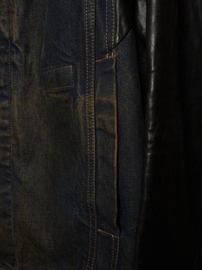 Close-up detail of a dark indigo denim jacket with contrast stitching and a black leather panel.