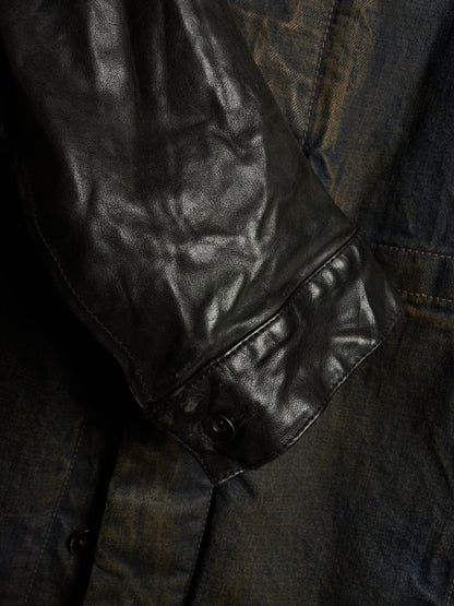 Close-up detail of a dark leather jacket sleeve with a snap-button cuff, layered over a distressed dark blue denim fabric.