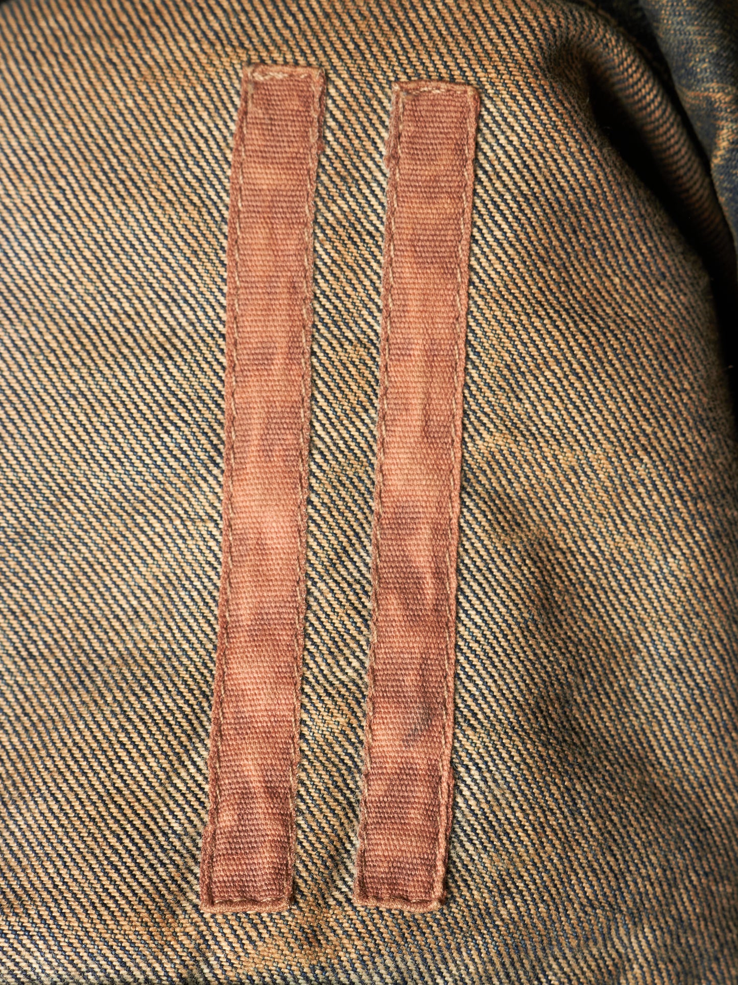 Close-up of a textured tweed fabric in brown and beige with two vertical rose-gold metal loops attached near the center.