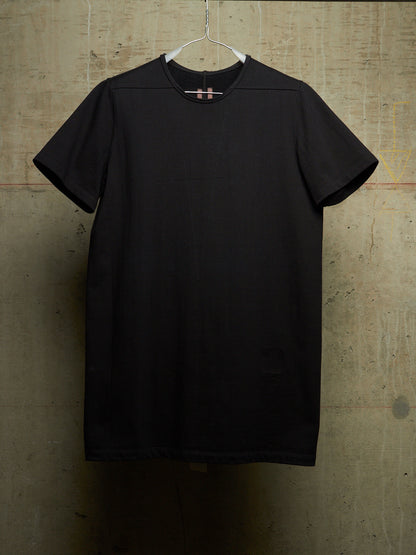 A black short-sleeve crewneck t-shirt hanging on a white plastic hanger against a textured concrete wall.