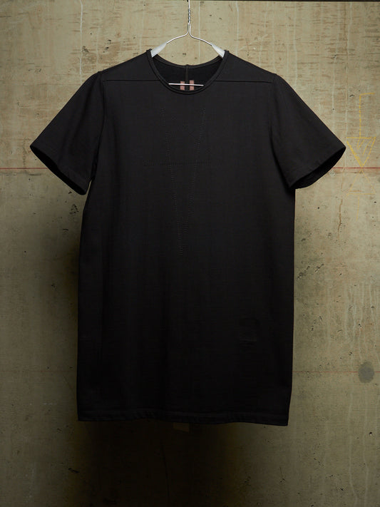 A black short-sleeve crewneck t-shirt hanging on a white plastic hanger against a textured concrete wall.
