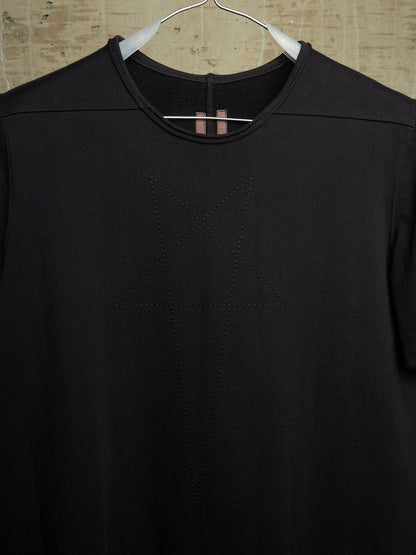 A black short-sleeve crewneck top hanging on a white hanger against a textured beige wall. The front features a subtle tonal geometric star design stitched or printed in the center.