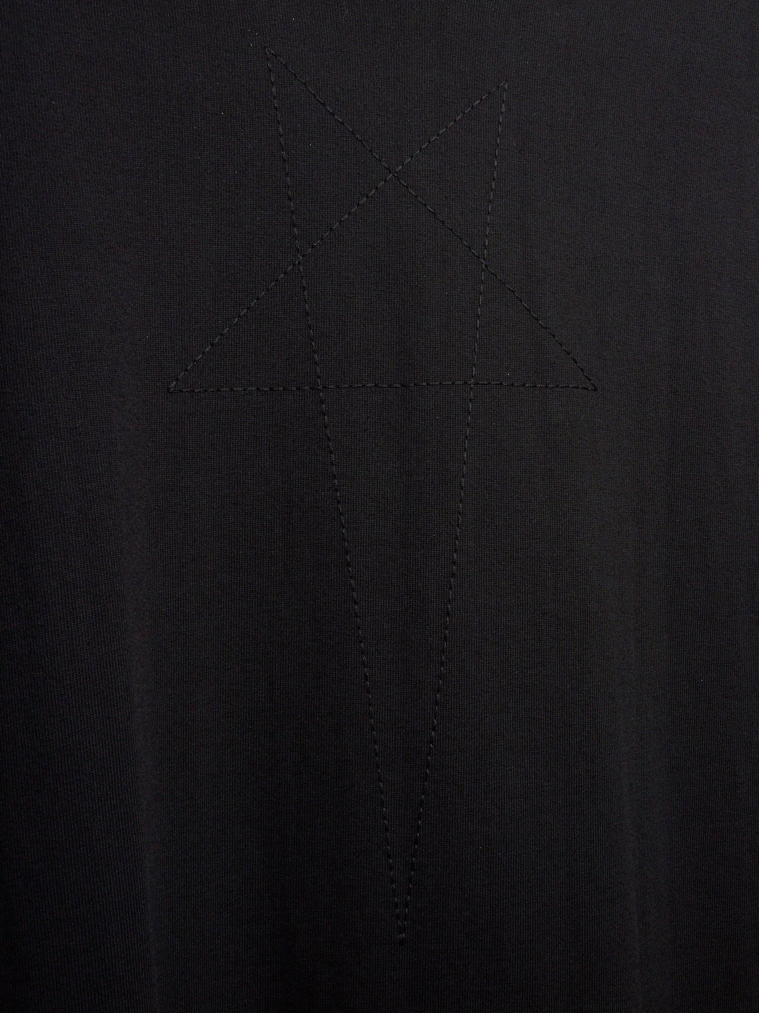 Close-up of a black ribbed knit fabric with a tonal embroidered or stitched star-like geometric motif in the center.
