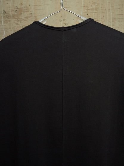 A black long-sleeve knit top hanging on a metal hanger against a textured beige wall, showing the back view with a central seam.