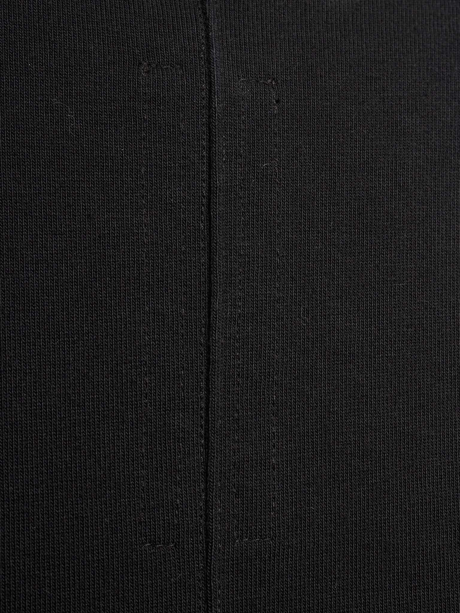 Close-up of a black textured knit fabric with a central seam running vertically.