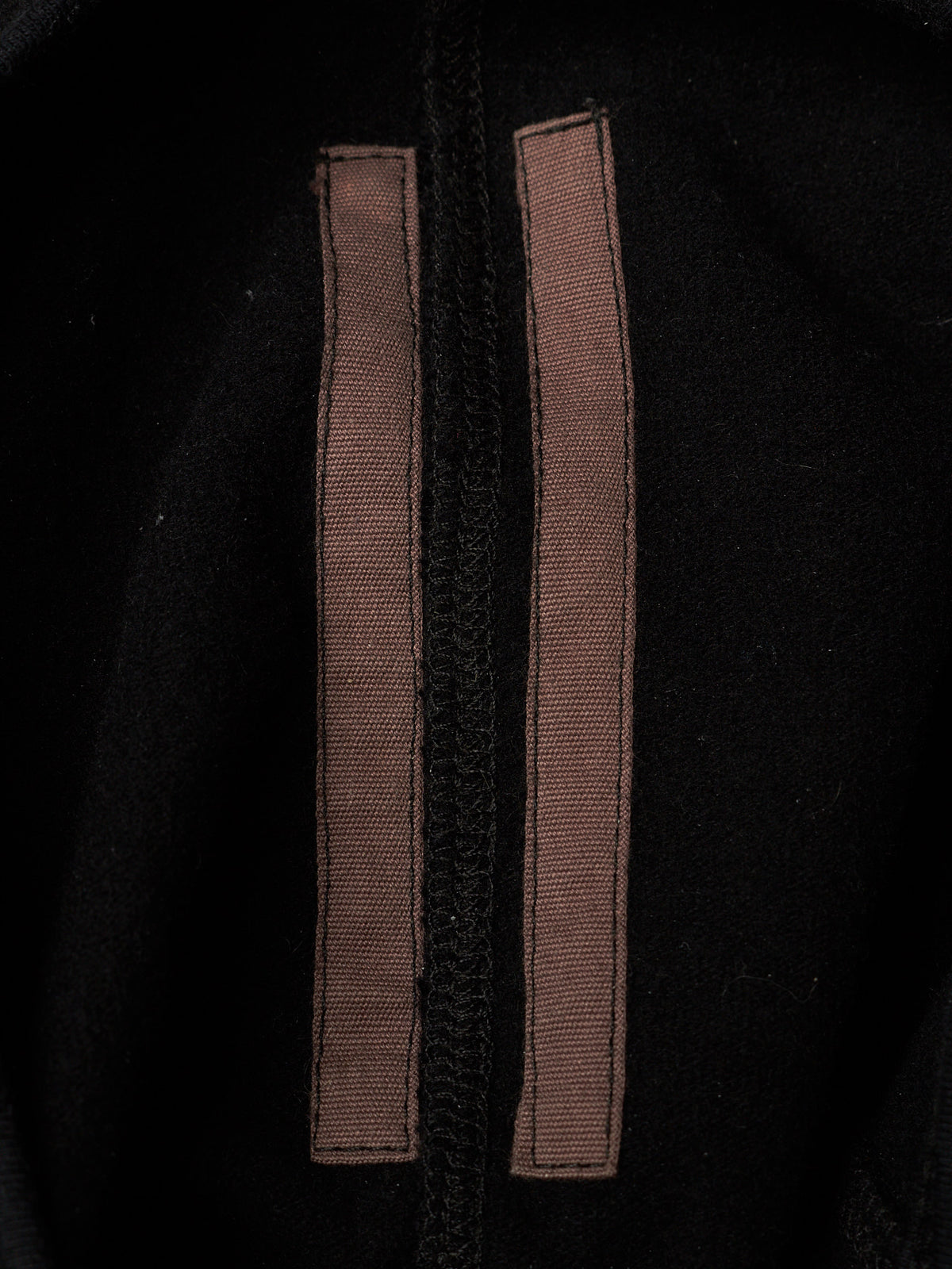 Close-up of a black garment featuring two vertical brown fabric tabs or straps stitched parallel to a central black zipper.