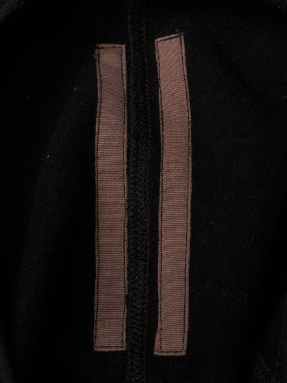 Close-up of a black garment featuring two vertical brown fabric tabs or straps stitched parallel to a central black zipper.