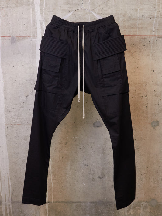 Black cargo pants on a hanger against a textured wall.
