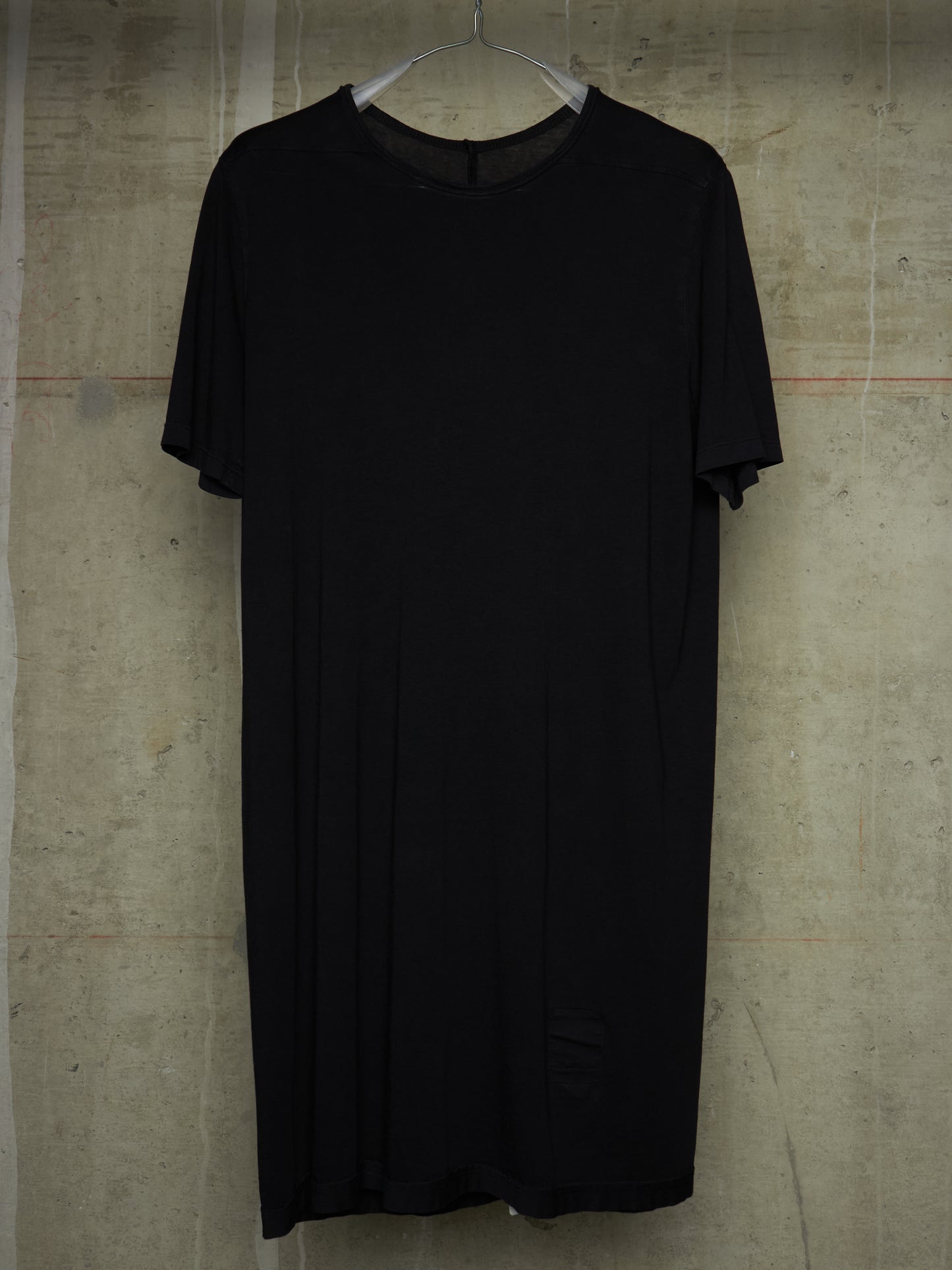 A black short-sleeve t-shirt dress hanging on a metal hanger against a textured concrete wall.