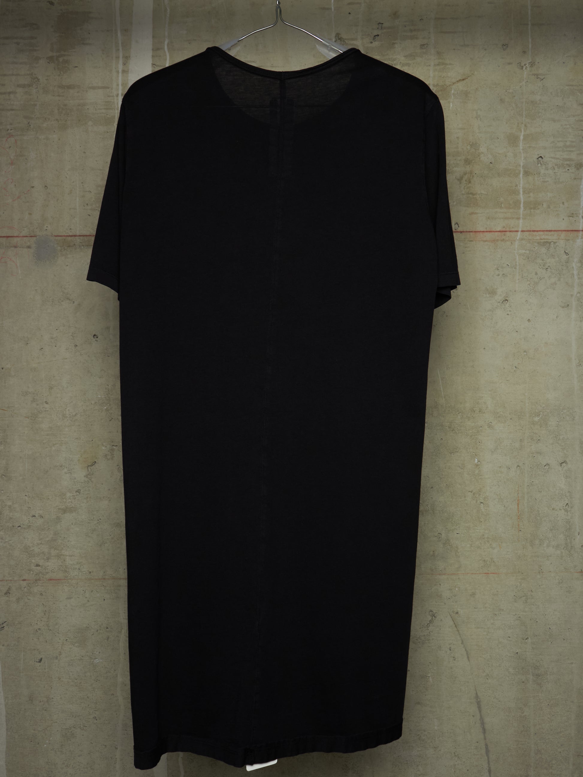 A black short-sleeve dress with a sheer V-neckline, hanging on a metal hanger against a textured concrete wall.