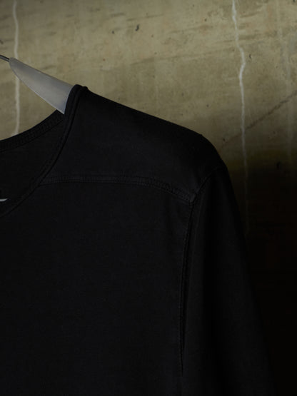 A close-up of a black crewneck sweatshirt hanging on a white hanger against a textured concrete wall.