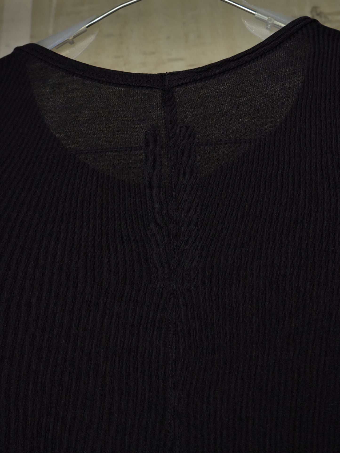 Close-up of a black knit top hanging on a clear plastic hanger, showing the back neckline and center seam.
