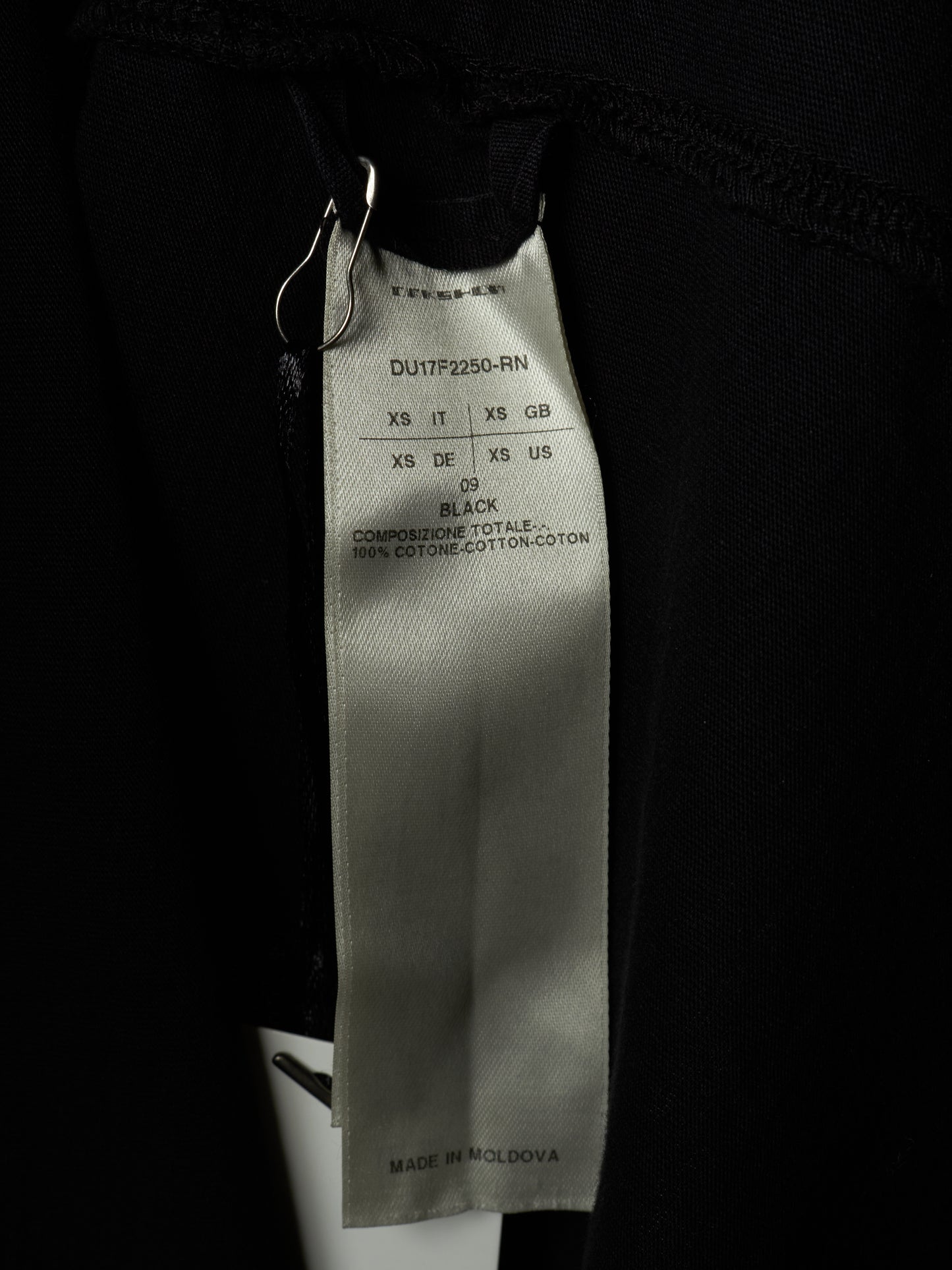 Close-up of a black garment's interior label showing the brand TOMSAM and size information for black cotton fabric.