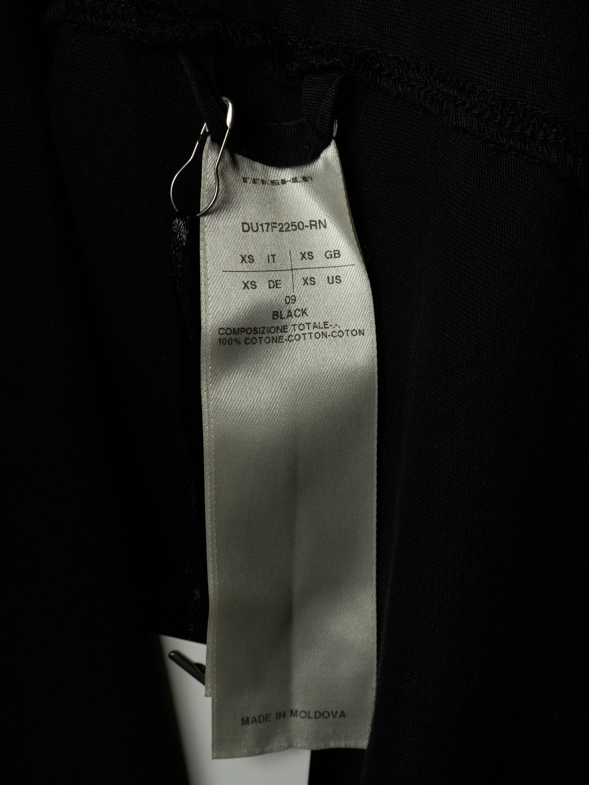 Close-up of a black garment's interior label showing the brand TOMSAM and size information for black cotton fabric.