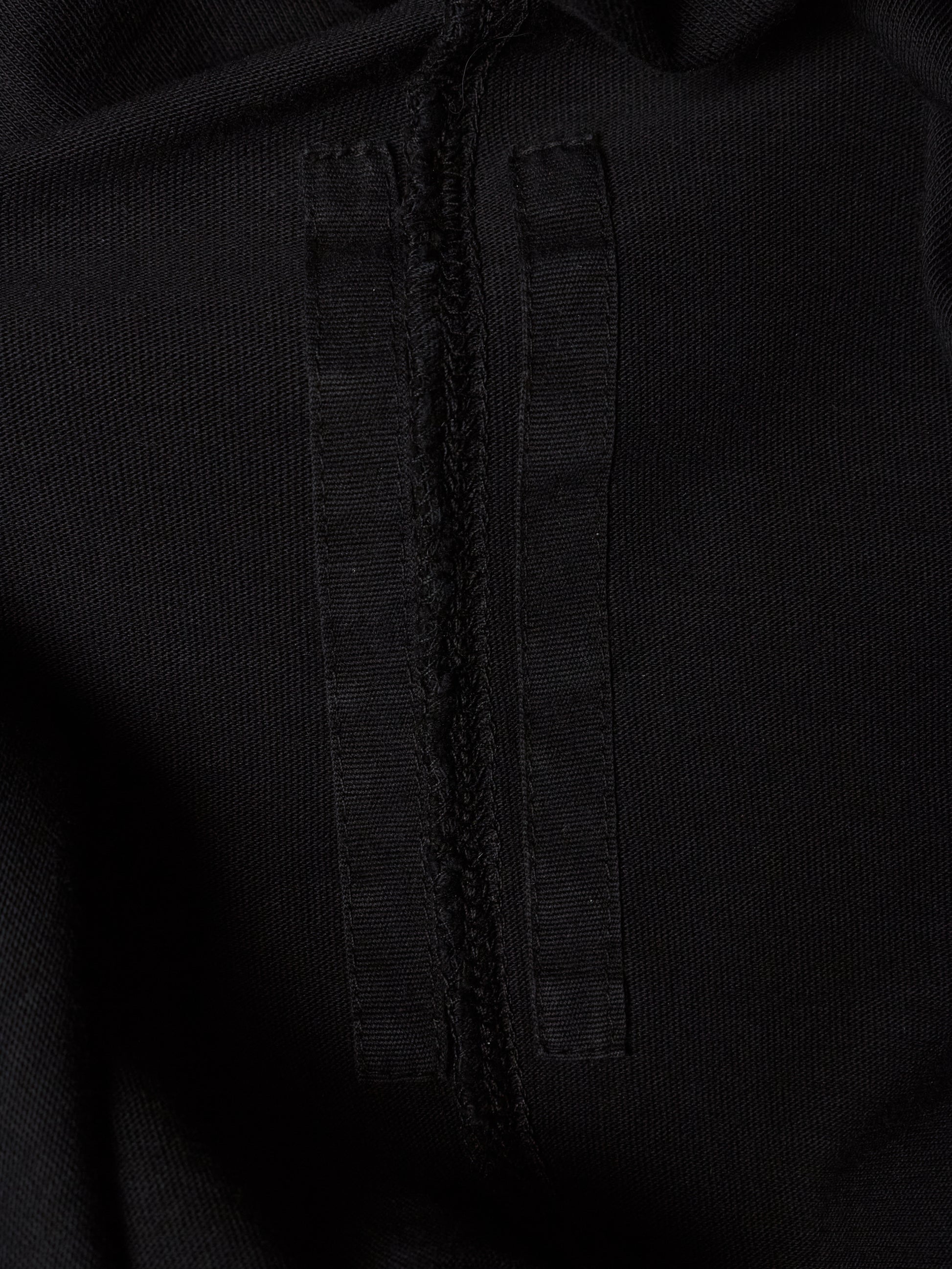 Close-up detail of a black textured fabric garment showing a central seam and a vertical stitched tab.