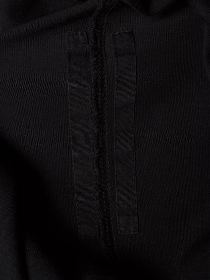 Close-up detail of a black textured fabric garment showing a central seam and a vertical stitched tab.