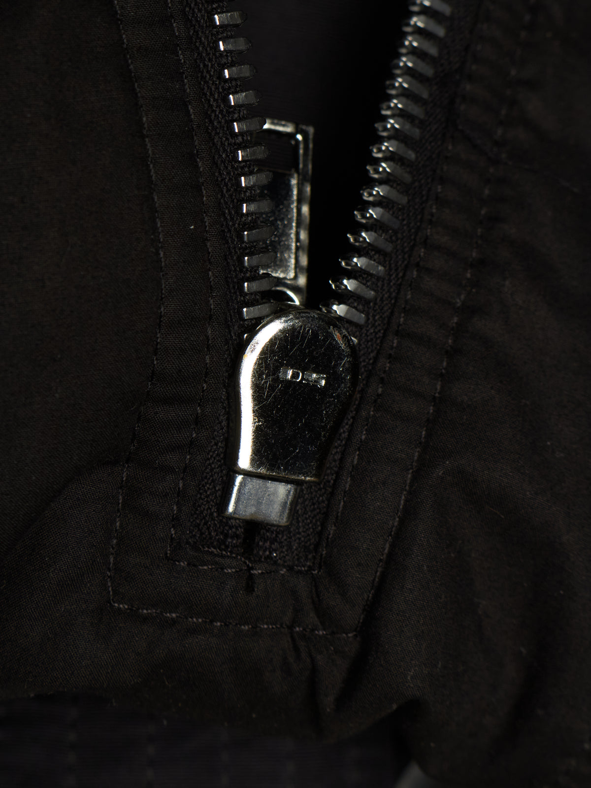 Close-up of a black zipper with a silver metal pull tab on a black fabric garment.