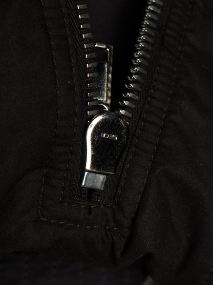 Close-up of a black zipper with a silver metal pull tab on a black fabric garment.