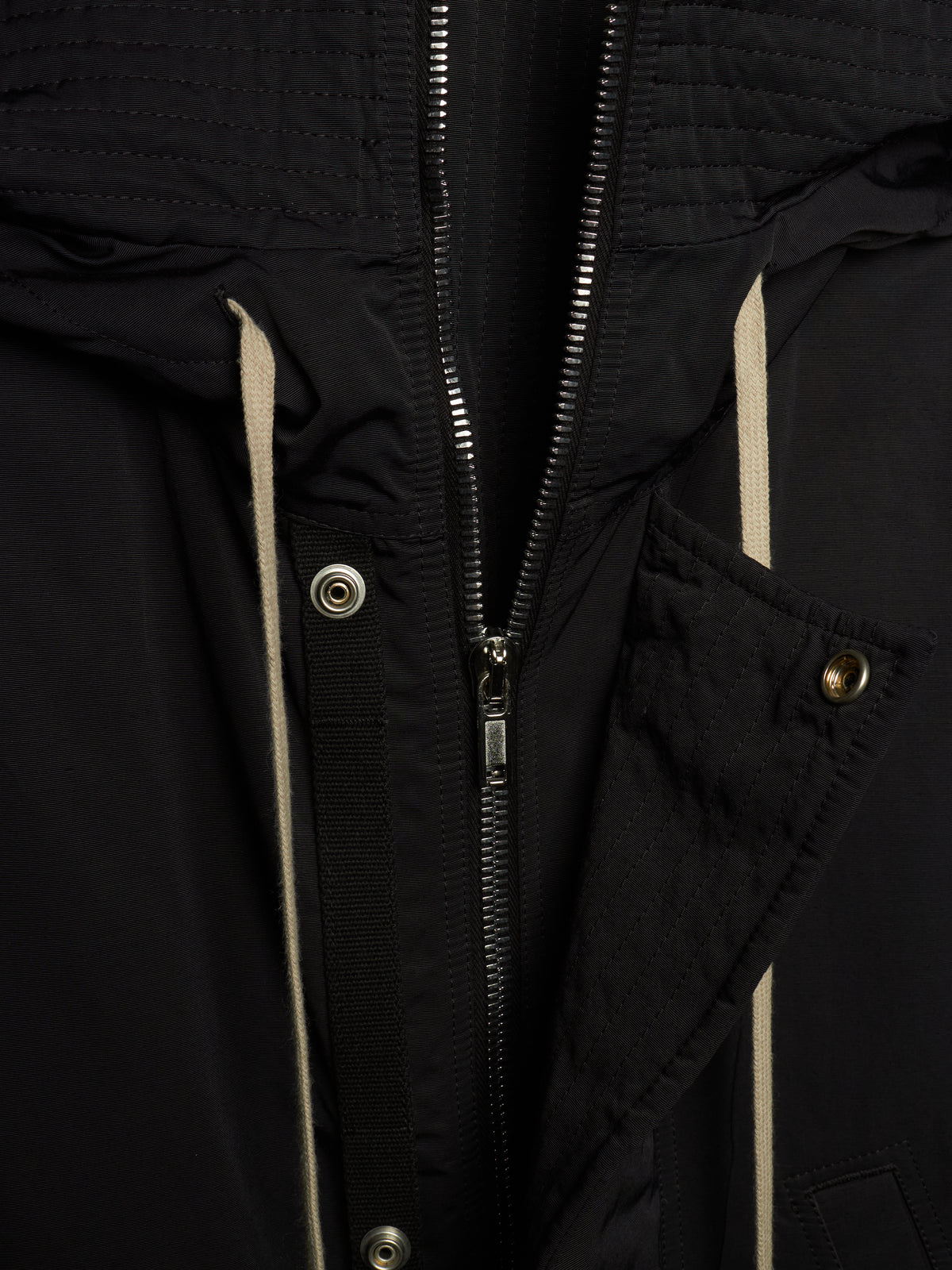 Close-up of a black jacket with a central zipper, silver-tone snaps, and light beige piping details.