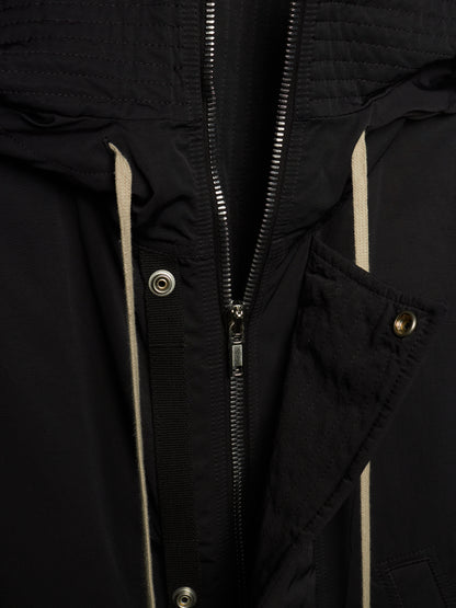 Close-up of a black jacket with a central zipper, silver-tone snaps, and light beige piping details.