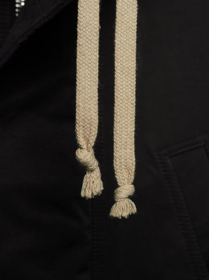 Close-up of a black garment with thick beige drawstrings knotted at the bottom, showing fabric texture and stitching details.