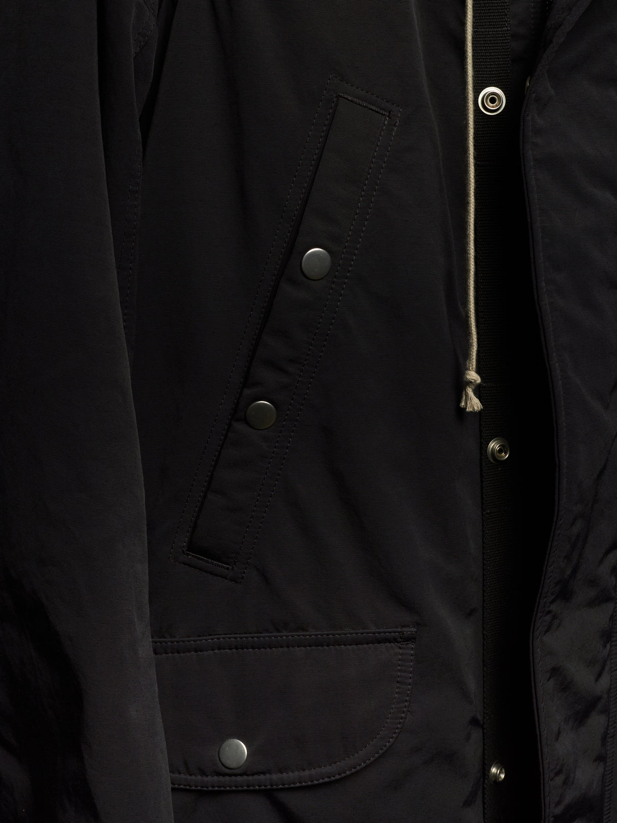 Close-up of a black jacket with silver snap buttons, a drawstring, and a quilted inner lining.