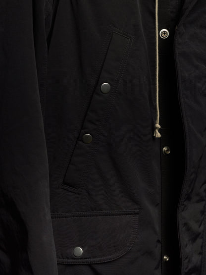 Close-up of a black jacket with silver snap buttons, a drawstring, and a quilted inner lining.