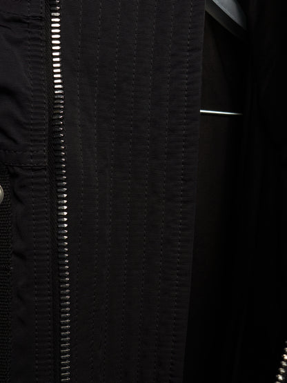 Close-up detail of a black jacket featuring a prominent silver zipper running vertically down the front, with textured stitching and a dark interior lining.