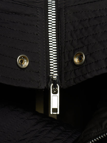 Close-up of a black quilted jacket featuring a central silver metal zipper, two matching snap buttons on the flap, and a dark interior lining.