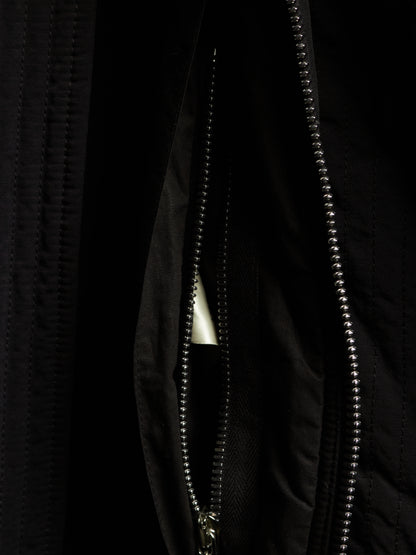 Close-up of a black quilted jacket with a silver metal beaded zipper and a small white triangular tab visible inside the pocket.