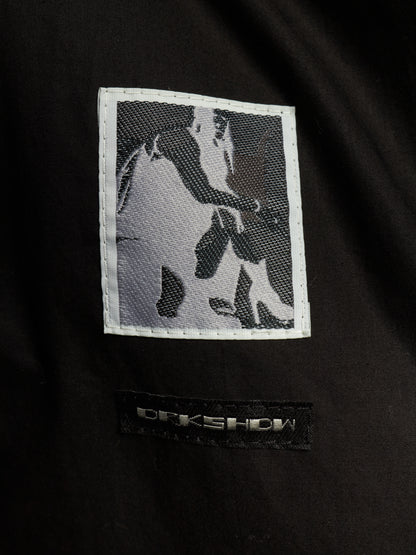 Close-up of a black garment featuring a rectangular embroidered patch with a grayscale horse design and a black brand label below reading ORKSHOW.