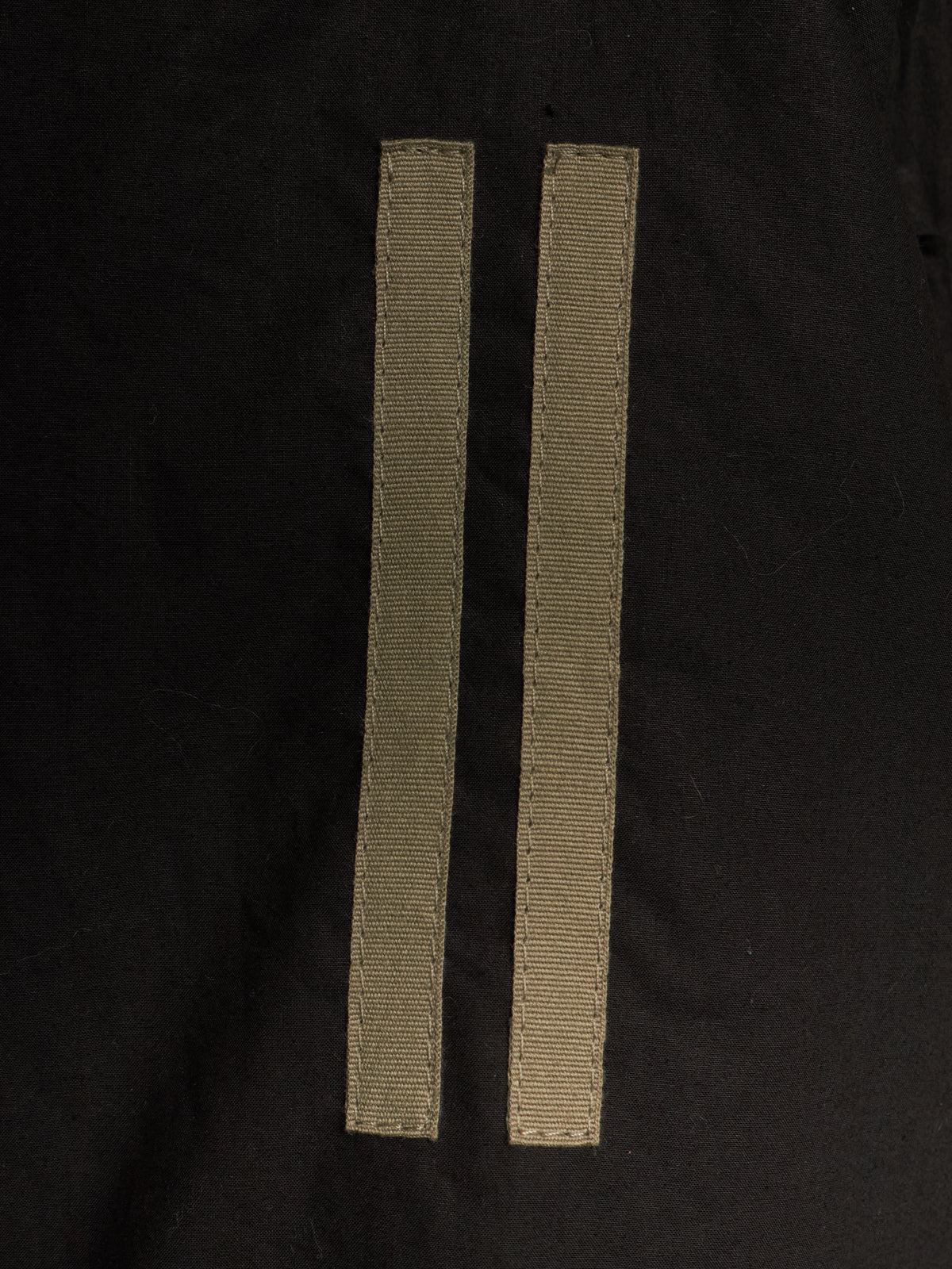 Two narrow beige woven ribbon strips laid flat on a black fabric background.