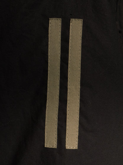 Two narrow beige woven ribbon strips laid flat on a black fabric background.