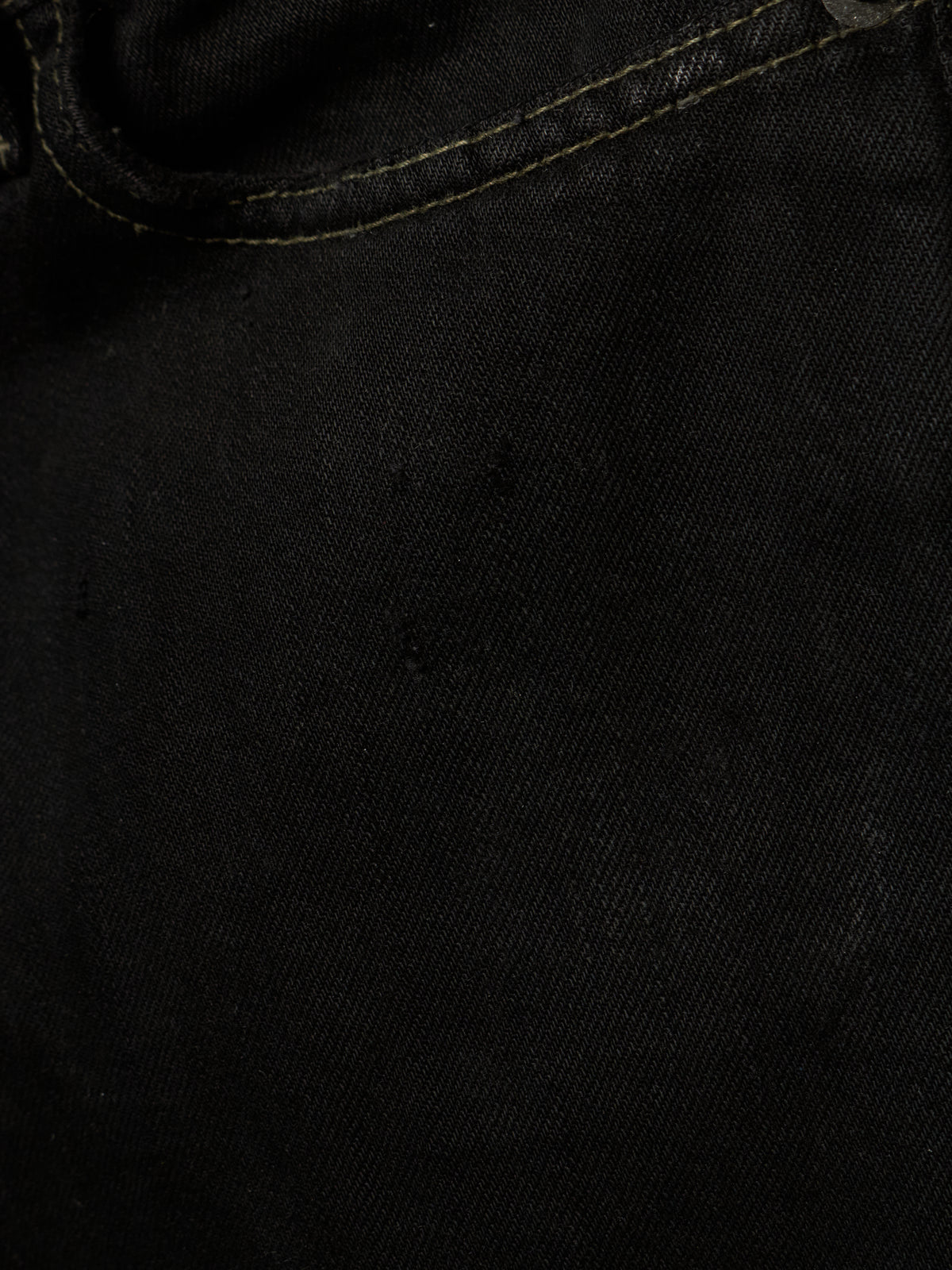 Close-up of black denim fabric with visible twill texture and a curved seam line.