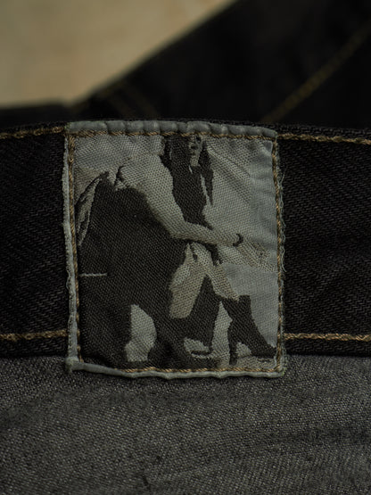 Close-up of a dark denim garment showing a rectangular fabric patch with a black-and-white photographic print of a person, bordered by tan contrast stitching.