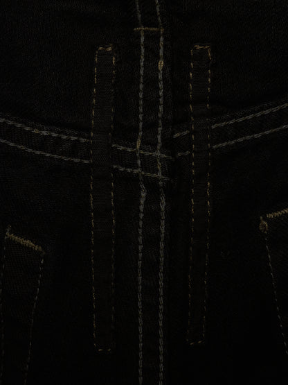 Close-up detail of black denim fabric with contrast light tan stitching, showing the front fly area and pocket edges.