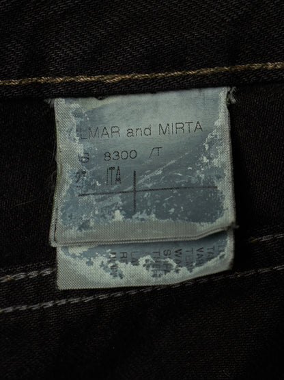 Close-up of a faded gray fabric garment label sewn onto dark black denim, showing the text 'LMAR and MIRT A 8300 / T' and size information.