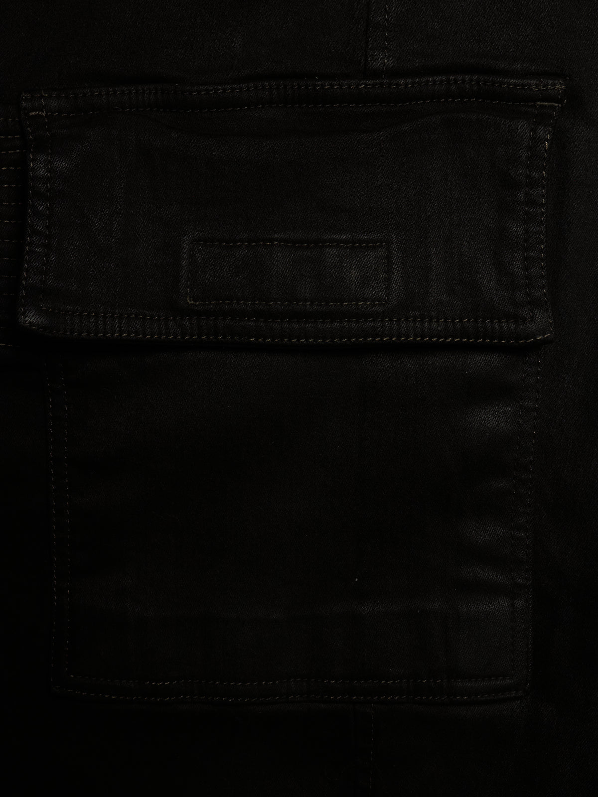 Close-up of a black leather or faux-leather pocket with visible stitching and a small rectangular patch on the flap.
